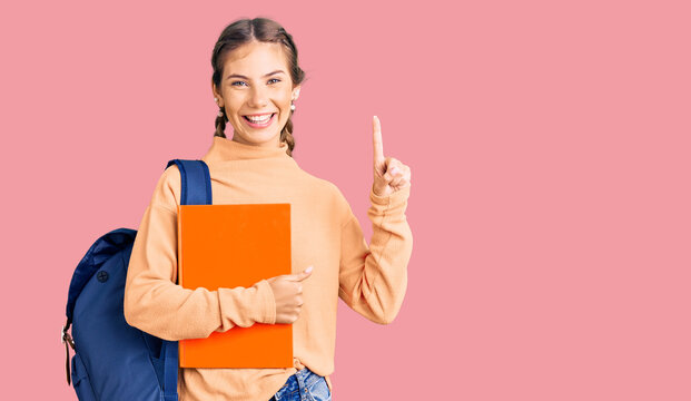 Beautiful caucasian woman with blonde hair wearing student backpack and holding book surprised with an idea or question pointing finger with happy face, number one