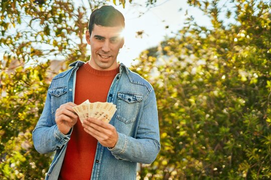 Young hispanic man smiling happy holding denmark krone banknotes at the city.