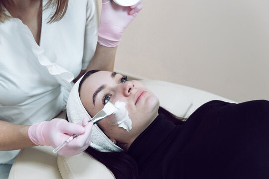 A Doctor In A White Coat Prepares A Client For Facial Cleansing. A Cosmetologist In A White Medical Gown Puts A Cosmetic Headband On A Client Before A Cosmetic Procedure.