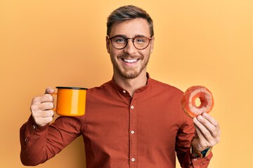 Fototapeta premium Handsome caucasian man eating doughnut and drinking coffee smiling and laughing hard out loud because funny crazy joke.
