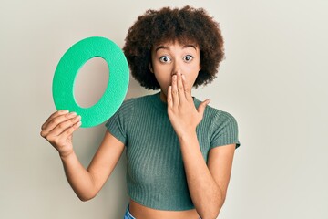 Young hispanic girl holding number zero covering mouth with hand, shocked and afraid for mistake....