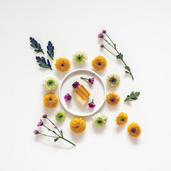 Flat lay cosmetic composition, oil bottles, wellness cosmetics, herbal ingredients, flowers on a white background, top view