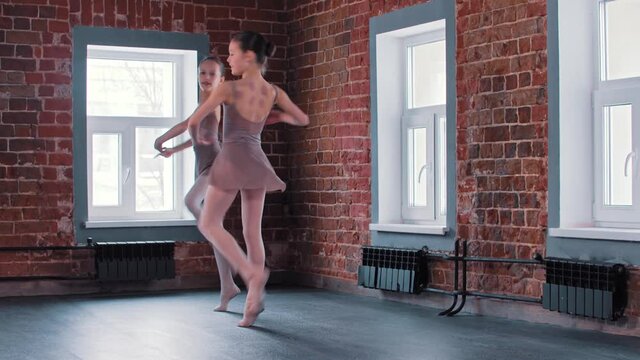 Two ballerina girls performing synchronized dancing movements and pirouettes in the studio 