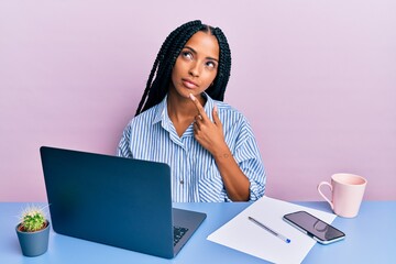 Beautiful hispanic woman working at the office with laptop serious face thinking about question...