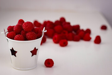 Red ripe and juicy raspberry in a small white bucket with stars