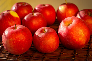 Several ripe red apples stand on a wicker basket illuminated by rays of the sun