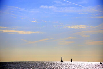 Backlight with silhouette of two lighthouses, on the horizon, and a boat, on the blue sea, in sunset light, Parc National des Calanques, Marseille, France