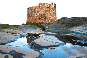 Authentic old stone watch tower on tidal coast, tidal pools, seaweed and warm sunset light.