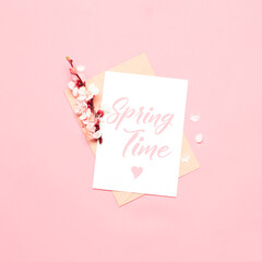 Fresh cherry flowers with white mockup card, Spring time text on pink background. Flat lay, top view.