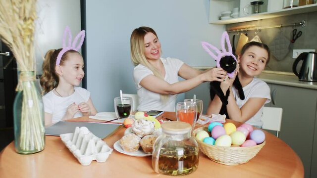 Happy family preparing for Easter. Cute little girls wearing bunny ears play with a black cat on Easter day.