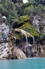 A rock in the French Mountains with a small waterfall flowing into the clear turquoise water - Lake Lac de Sainte-Croix, France