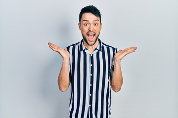 Fototapeta premium Young hispanic man wearing casual clothes celebrating crazy and amazed for success with arms raised and open eyes screaming excited. winner concept