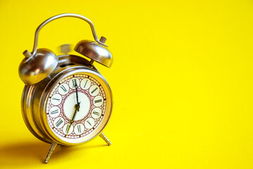 The old alarm clock rings on an isolated yellow background.