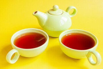 A green tea service made of teapot and two mugs with tea on an isolated yellow background.