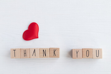 The word thank you on wooden cubes and a red heart on a light background with space for your text. Postcard, business card layout.