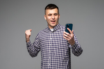 Excited Caucasian man look at smartphone happy get good text message isolated on grey studio background.