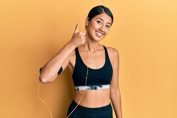 Beautiful asian young sport woman wearing sportswear and earphones smiling happy and positive,...