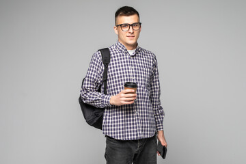 Attractive young man student with backpack and drinks coffee isolated on gray background