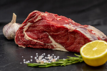 Fresh raw beef for steaks with spices and lemon on a black slate board.