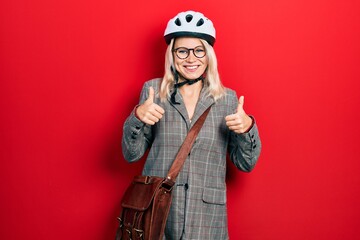 Beautiful caucasian blonde business woman wearing bike helmet success sign doing positive gesture with hand, thumbs up smiling and happy. cheerful expression and winner gesture.