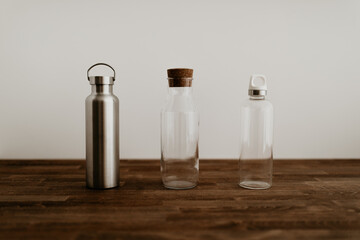 Three different type of eco friendly water bottles on wooden table with white background. Metal and glass water bottles. Zero waste, sustainable solution to avoid using plastic. 