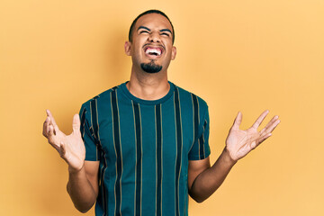 Young african american man wearing casual clothes crazy and mad shouting and yelling with aggressive expression and arms raised. frustration concept.