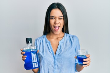 Young hispanic girl holding mouthwash for fresh breath winking looking at the camera with sexy...