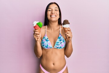 Naklejka premium Young latin woman wearing bikini holding ice cream smiling with a happy and cool smile on face. showing teeth.
