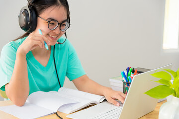 Asian young woman student with glasses headphones teenage girl study happy sitting looking video conference on a laptop computer, University class online internet learning distance education from home