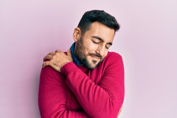 Young hispanic man wearing casual clothes hugging oneself happy and positive, smiling confident....