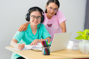 Happy family two Asian woman looking up mother parent is a teacher advice instruction daughter teenage girl student online study use a laptop computer education from university class learning at home