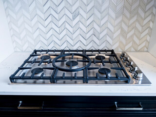 view of an iron stove top with stainless steel knobs inside a kitchen with a nice backsplash