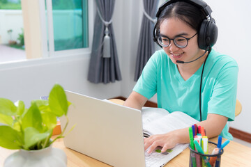 Portrait Asian young woman student with glasses headphones to study class college online learning internet education teenage girl is smiling use laptop keyboard looking computer work remotely at home