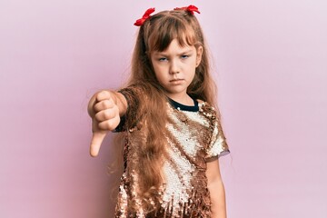 Little caucasian girl kid wearing festive sequins dress looking unhappy and angry showing rejection and negative with thumbs down gesture. bad expression.