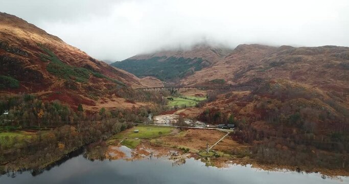 4k aerial footage of Glenfinnan monument, viaduct and mountains with mist. Autumn colours. Slow pan forwards.