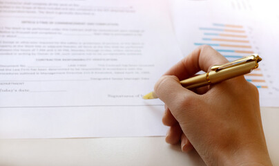 Young business woman signs a business contract on the background of economic charts while sitting at the table. Business and finance concept. Selective focus.