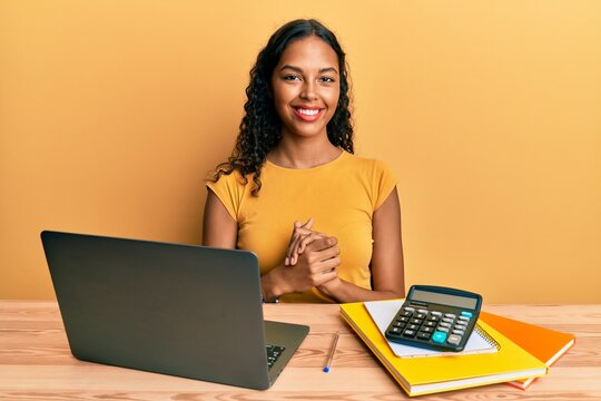 Young african american girl working at the office with laptop and calculator with hands together and crossed fingers smiling relaxed and cheerful. success and optimistic