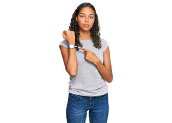 Young african american girl wearing casual clothes in hurry pointing to watch time, impatience, looking at the camera with relaxed expression