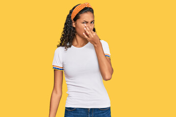 Young african american girl wearing casual clothes smelling something stinky and disgusting,...