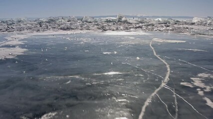 Flying low over the ice of a frozen lake. Approaching ice hummocks and blocks of broken pieces of ice with an opening view of people skating in the distance