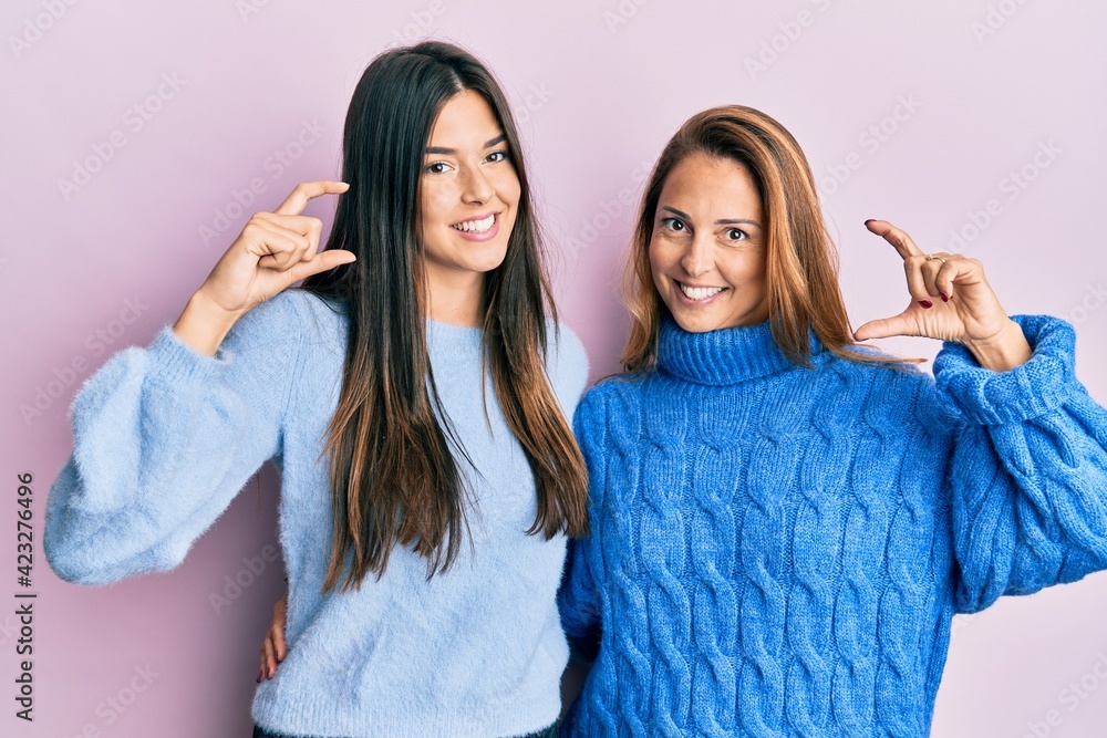 Sticker Hispanic family of mother and daughter wearing wool winter sweater smiling and confident gesturing with hand doing small size sign with fingers looking and the camera. measure concept.