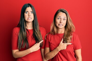 Hispanic family of mother and daughter wearing casual clothes over red background pointing aside worried and nervous with forefinger, concerned and surprised expression