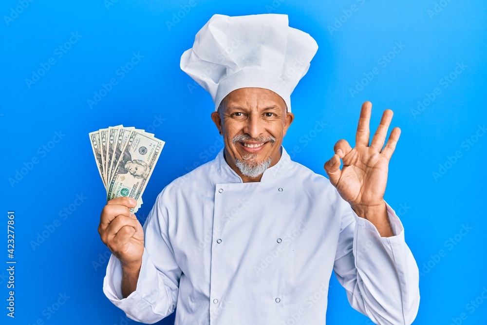 Sticker Middle age grey-haired man wearing professional cook uniform holding usa dollars banknotes doing ok sign with fingers, smiling friendly gesturing excellent symbol