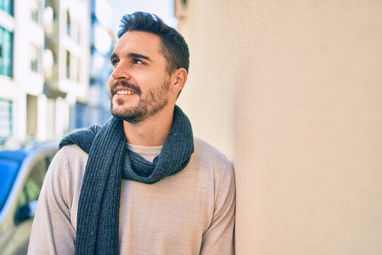 Young hispanic man smiling happy wearing scarf leaning on the wall at the city.
