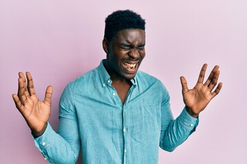 Handsome black man wearing casual clothes celebrating mad and crazy for success with arms raised...