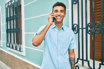 Young latin man smiling happy using smartphone walking at the city.