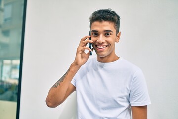 Young latin man smiling happy talking on the smartphone walking at the city.