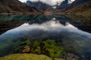 A polarizing filter shows rocks and green grass in Lake Carhuacocha during a reflection and sunrise in the Cordillera Huayhuash of the Andes Mountains in Peru.     