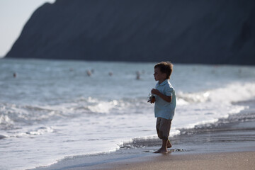 a child in wet shorts and a turquoise T shirt looks at the sea in the distance