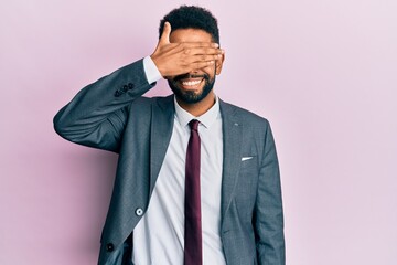 Handsome hispanic business man with beard wearing business suit and tie smiling and laughing with hand on face covering eyes for surprise. blind concept.